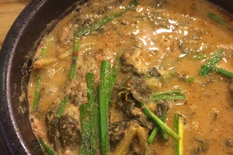 A steaming bowl of chueotang, thick Korean ground-loach soup with green vegetables and perilla
