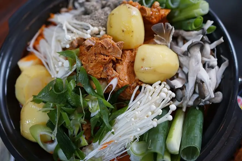 A bubbling pot of gamjatang, Korean pork back-bone stew with whole potatoes, perilla leaves, green onions and enoki mushrooms