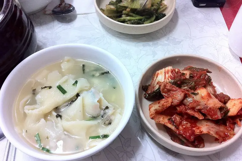 A bowl of sujebi, Korean hand-torn dough flake soup with zucchini and potato, served with a side of kimchi